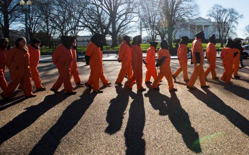 Activists dressed in orange jumpsuits representing detainees in the U.S.-run detention center at Guantanamo Bay, Cuba, protest in front of the White House (CNS)