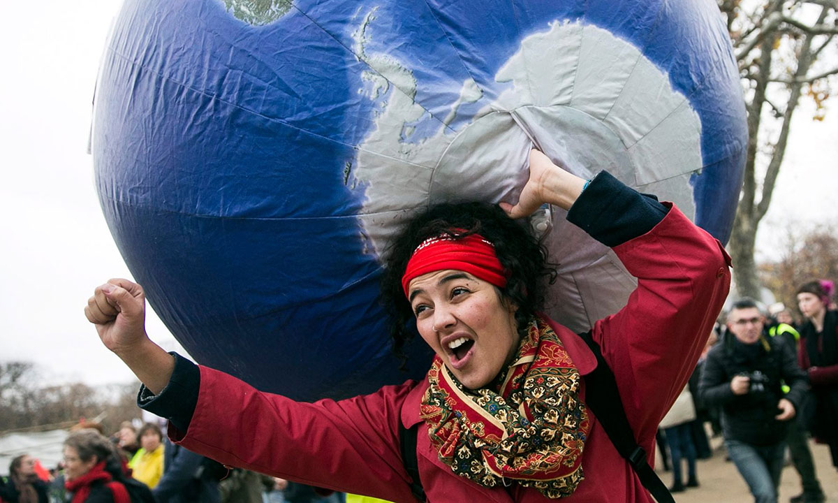 žena koja protestuje, u levoj ruci ima balon planetu Zemlju, desna ruka je stisnuta u pesnicu