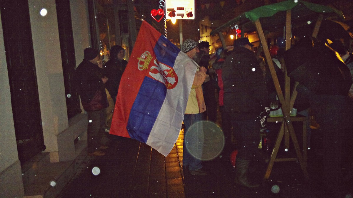ljudi na ulici sa zastavom Srbije