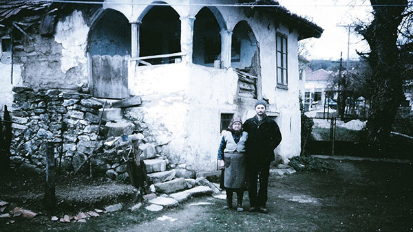 crno-bela fotografija: starica i mladić ispred stare kuće