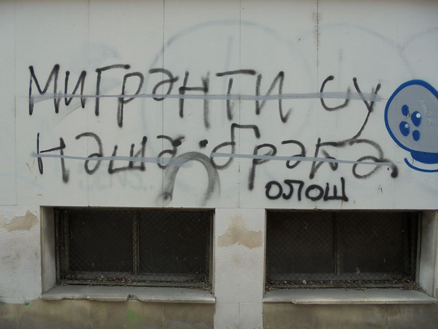 Precrtan grafit na kojem piše: Migranti su naša braća, i ispod njega dopisano Ološ